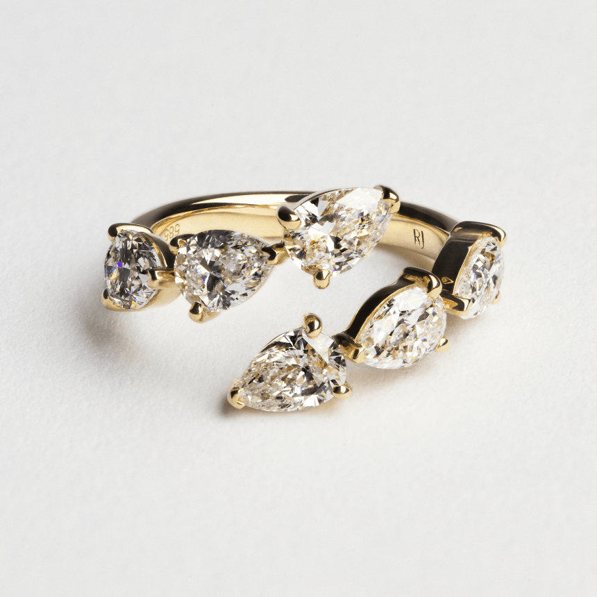 Gold ring with pear-shaped diamonds on a light gray background
