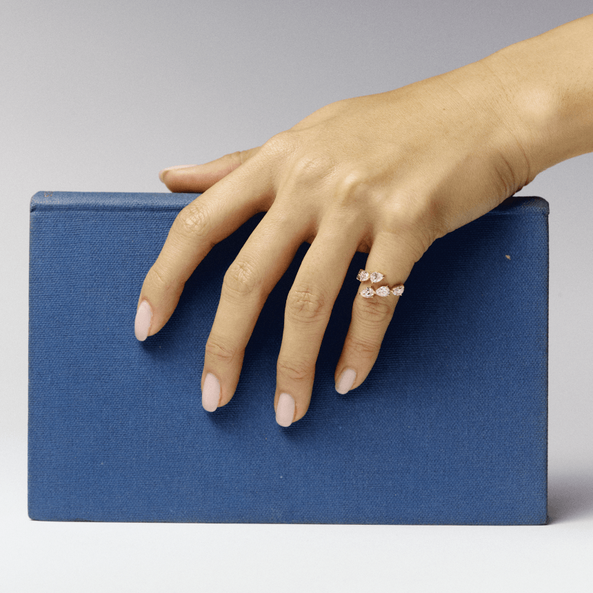 Hand with a gold diamond pear wrap ring on a blue book against a gray background
