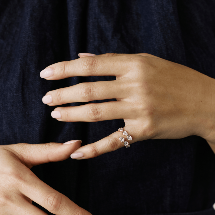 Close-up of a hand wearing a gold pear cut diamond wrap ring against a dark background