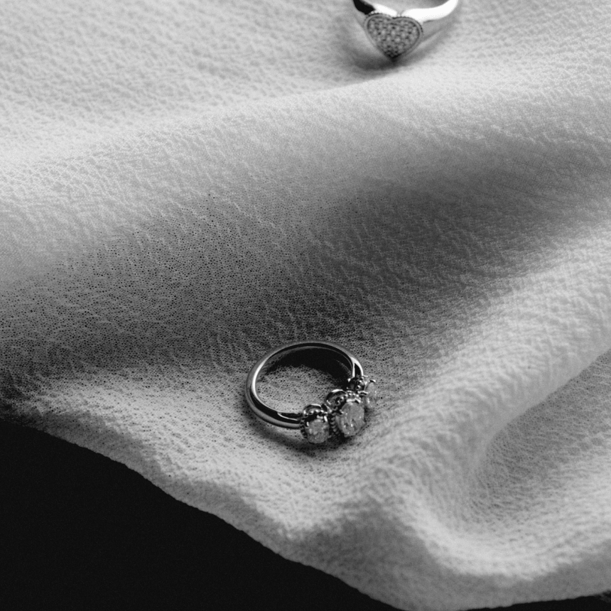 Two white gold rings oval trilogy and heart signet pinky on white fabric textured background