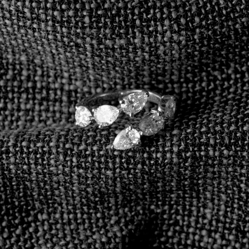 White gold diamond ring with pear-shaped diamonds on a textured black fabric background