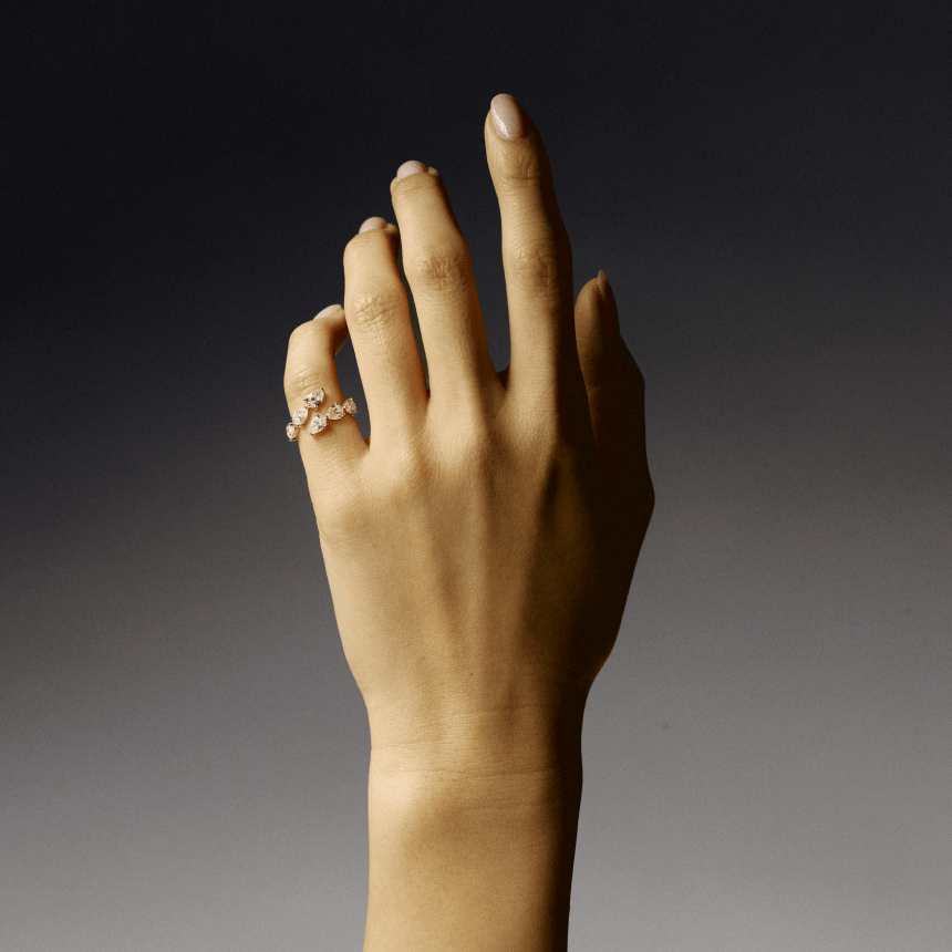 Hand wearing a gold pear cut diamond wrap ring on a gradient background