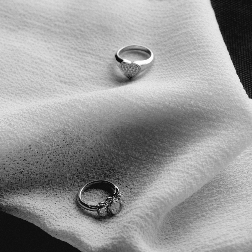 Two white gold diamond pinky rings on a textured white surface