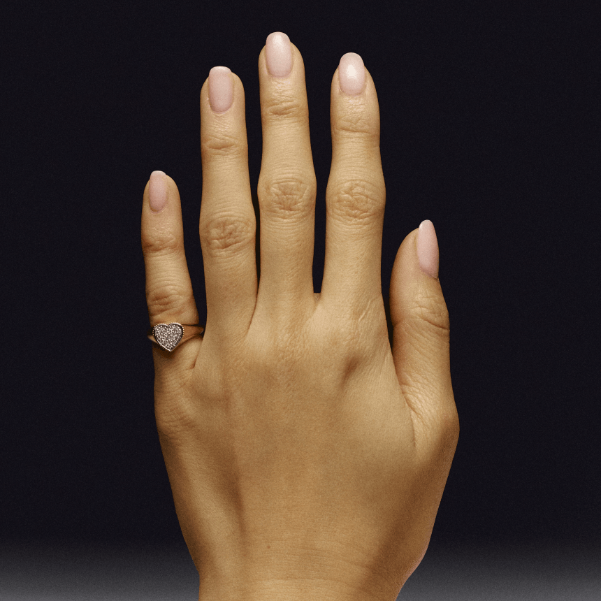 Hand wearing a gold heart-shaped pave diamond pinky signet ring on a black background