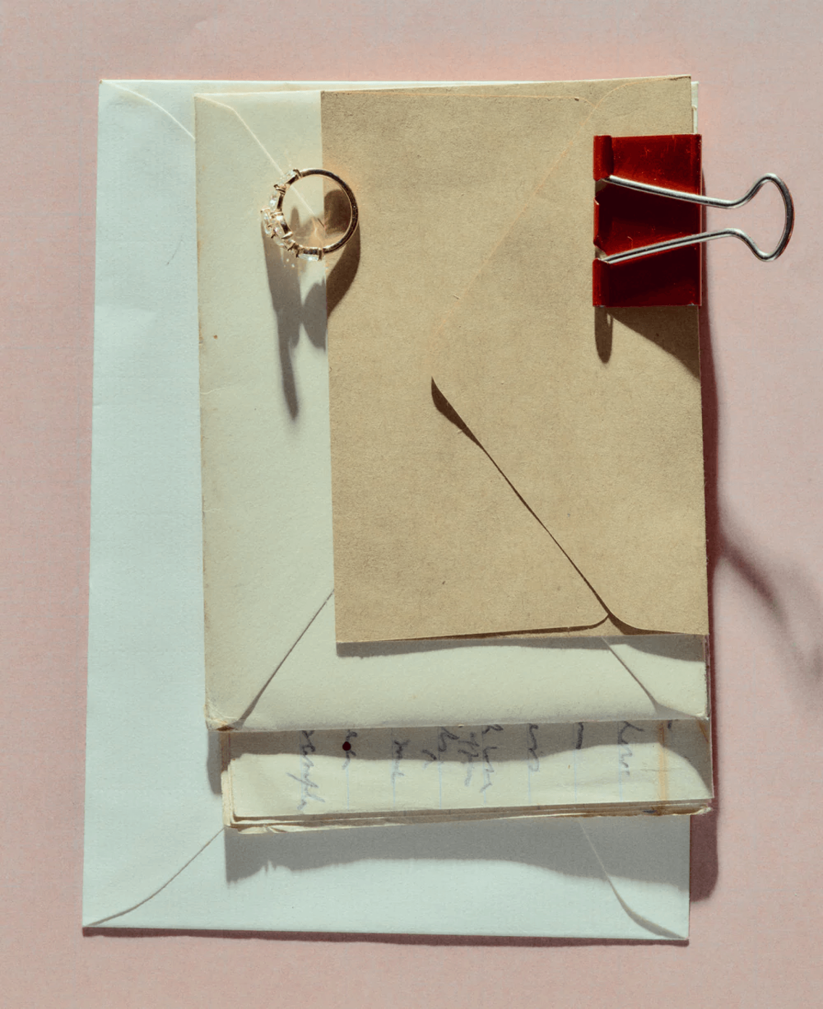 Stack of letters and envelopes with a ring on a pink background